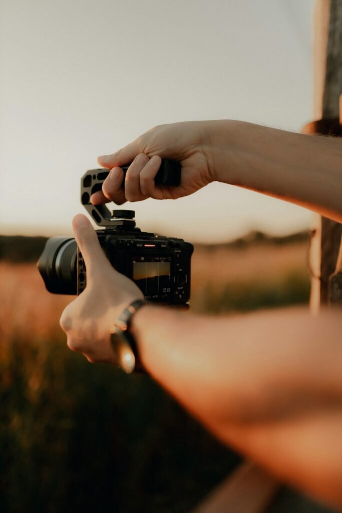 Manos sujetando una cámara con asa superior a contraluz al atardecer