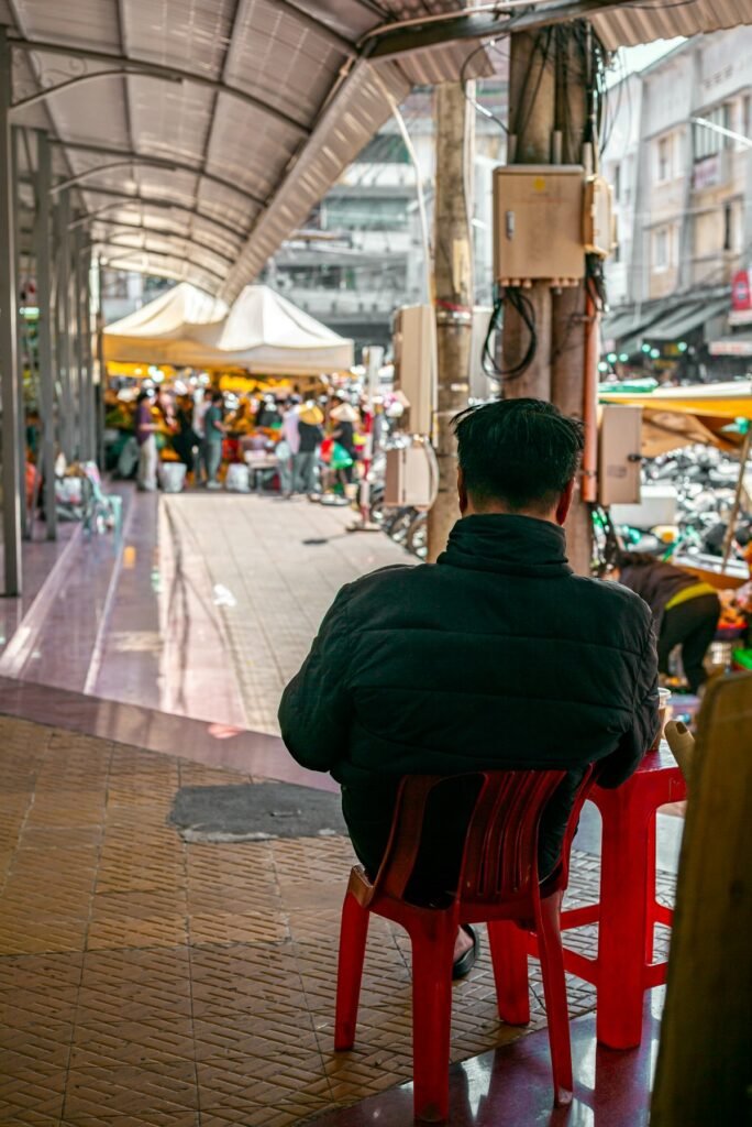 Hombre sentado en una silla roja de plástico observando un mercado cubierto