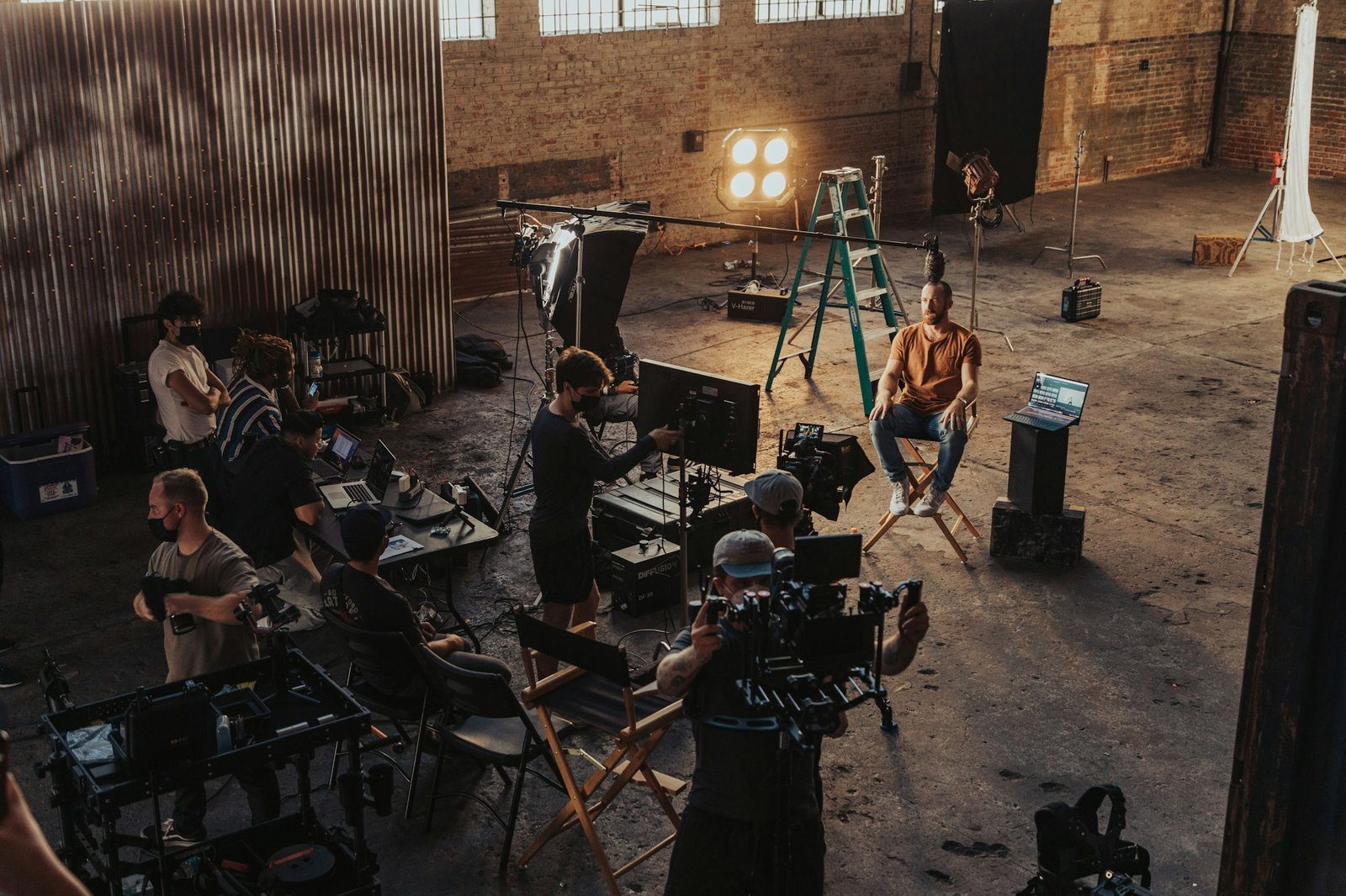 Equipo de rodaje grabando una entrevista en una nave industrial, con operador de cámara, focos y la persona entrevistada sentada